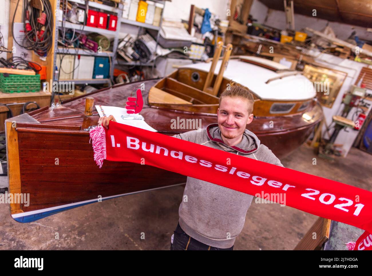 25 January 2022, Mecklenburg-Western Pomerania, Greifswald: Boat builder Florian Woll stands in the workshop of the museum shipyard with the winner's scarf as the current national winner in the performance competition of the German skilled crafts in the craft of boat building. The Chamber of Crafts of Eastern Mecklenburg-Western Pomerania (HWK) had previously presented the certificate and trophy at the Greifswald training company. According to the HWK, 58 companies with the boat and shipbuilding trade are registered in its jurisdiction. A total of 55 apprentices are being trained in the boatbu Stock Photo