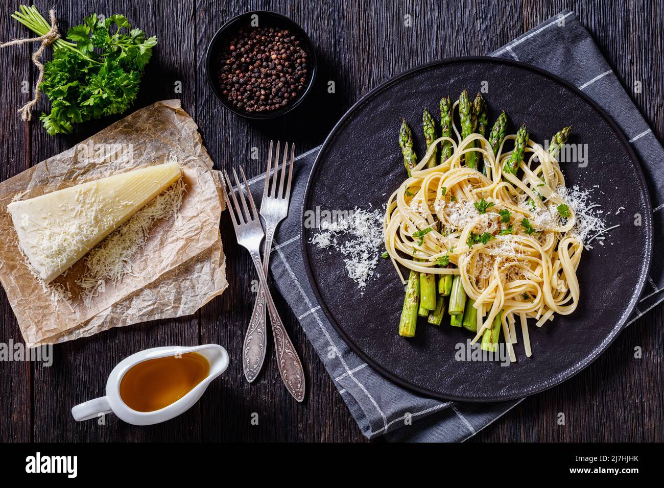roasted asparagus spears with spaghetti sprinkled with shredded pecorino cheese and parsley on black plate on dark wooden table with ingredients, hori Stock Photo