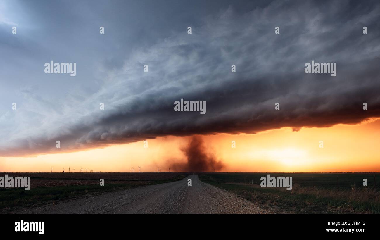 A landspout tornado spins beneath dramatic storm clouds at sunset near