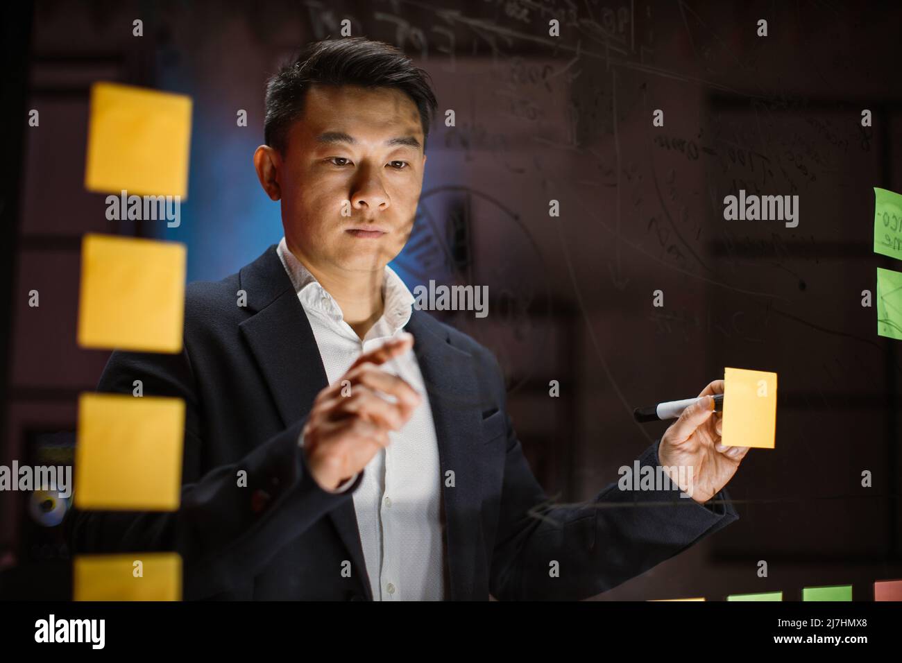View through the glass board of focused Asian businessman, thinking ...
