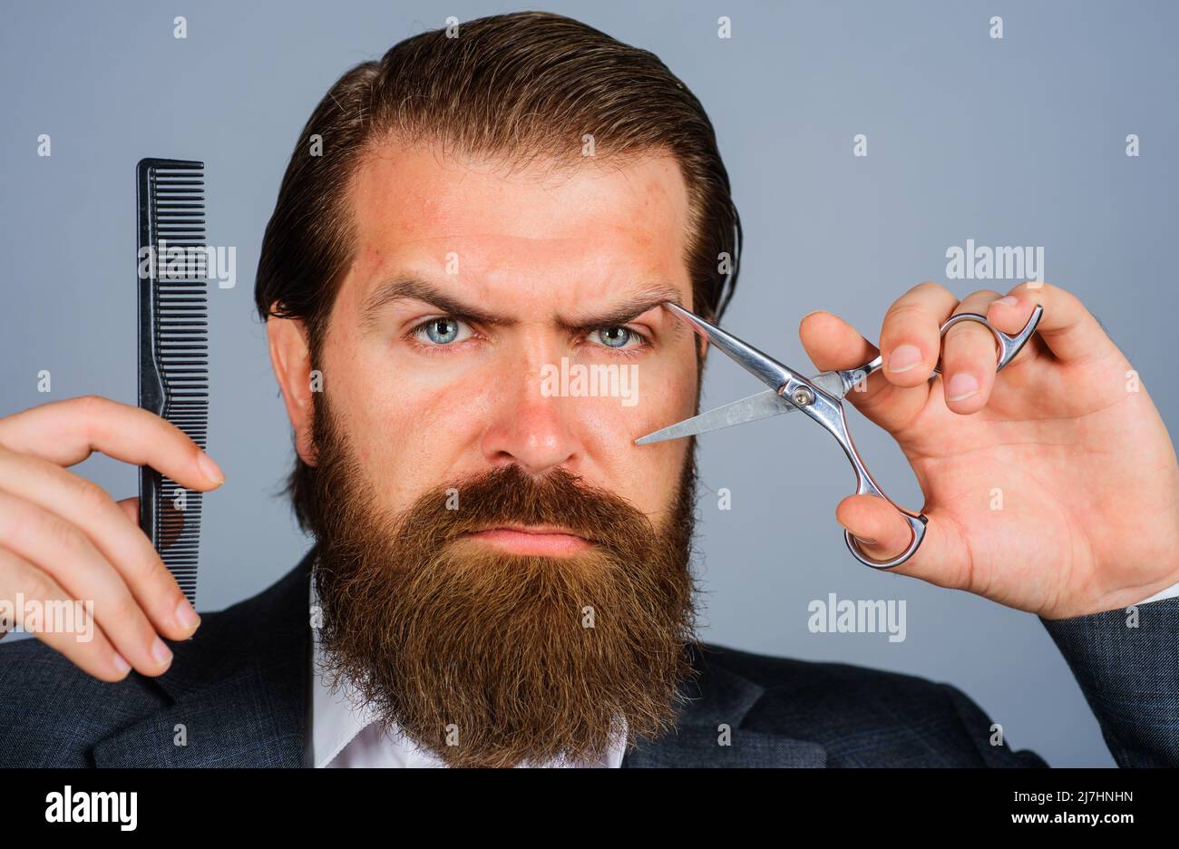 Barbershop advertising. Bearded man with scissors and comb. Male hairdresser with barber tools. Stock Photo