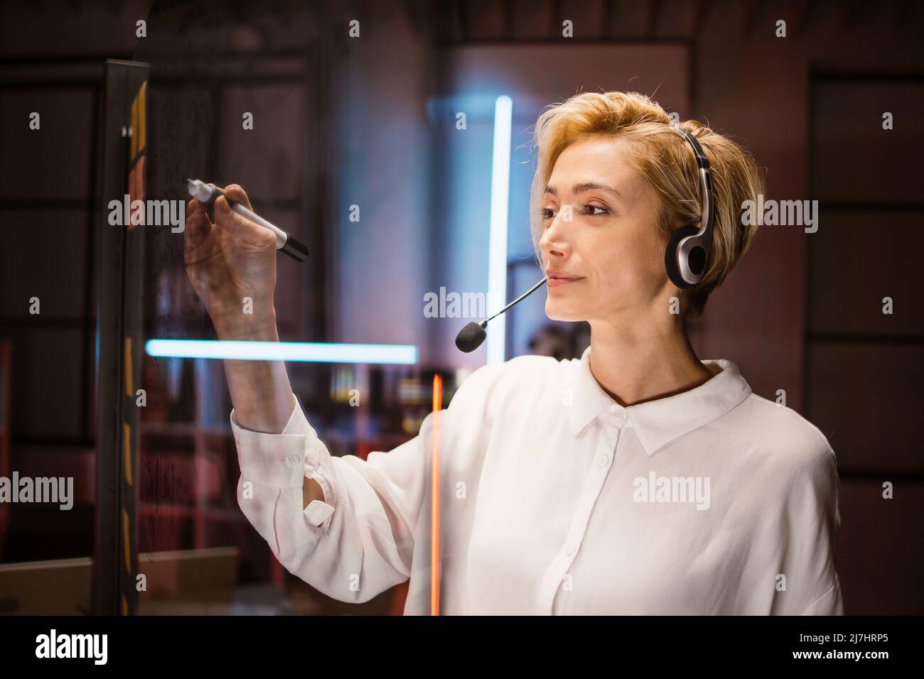 Close up side view of pleasant concentrated Caucasian female employee, managing working tasks or project operations, writing notes on glass transparent wall in office. Stock Photo