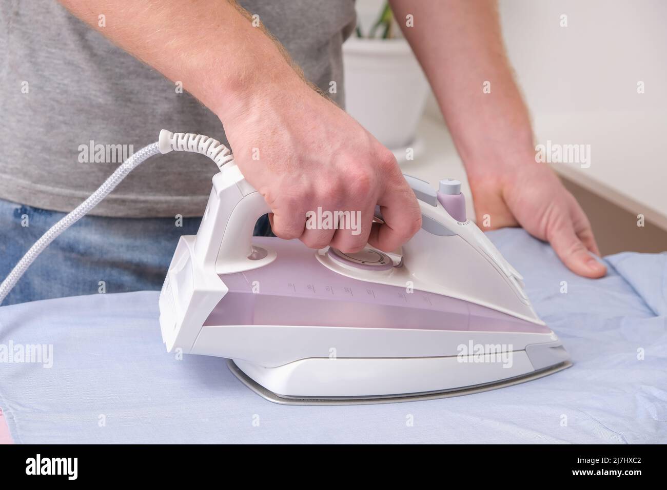 A man is ironing a shirt with an electric iron on an ironing board