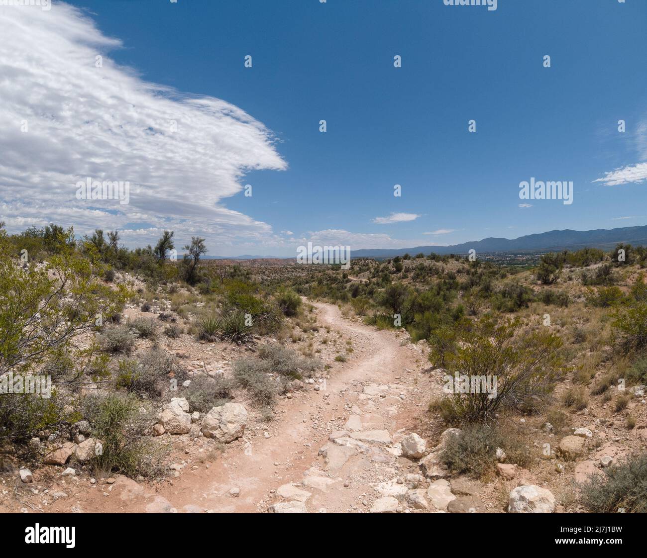 Rocky hiking path in the desert with a blue sky split by incoming clouds. Stock Photo