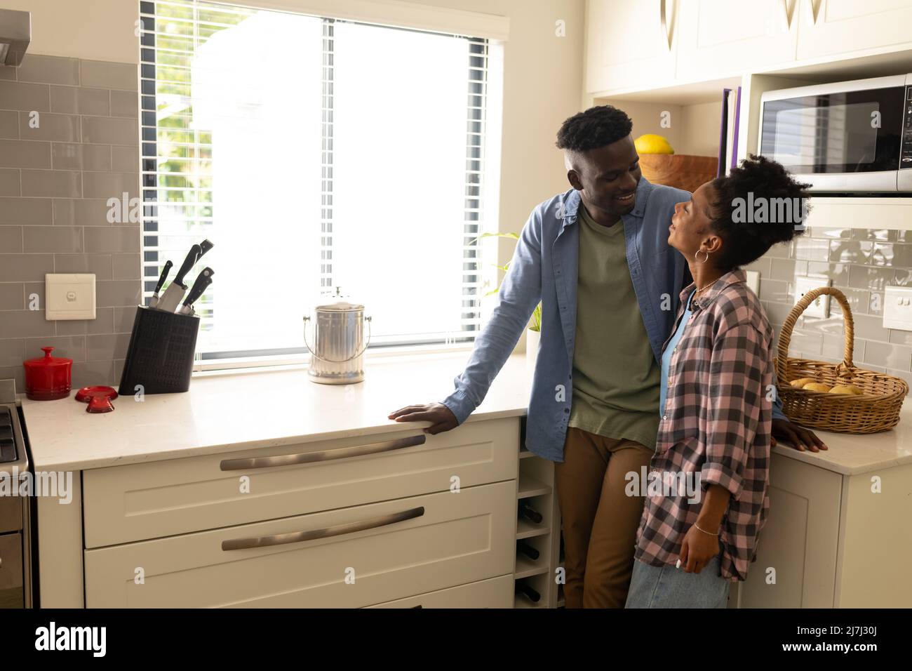 Smiling african american young couple looking at each other while standing by counter in kitchen Stock Photo