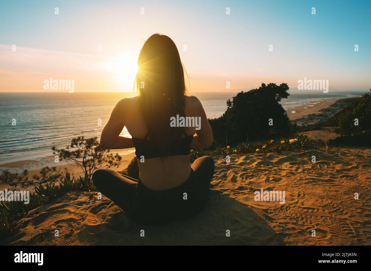 Woman practicing yoga and meditates on the mountain with ocean view at sunset. Young woman sitting in lotus pose outdoor in the nature Stock Photo