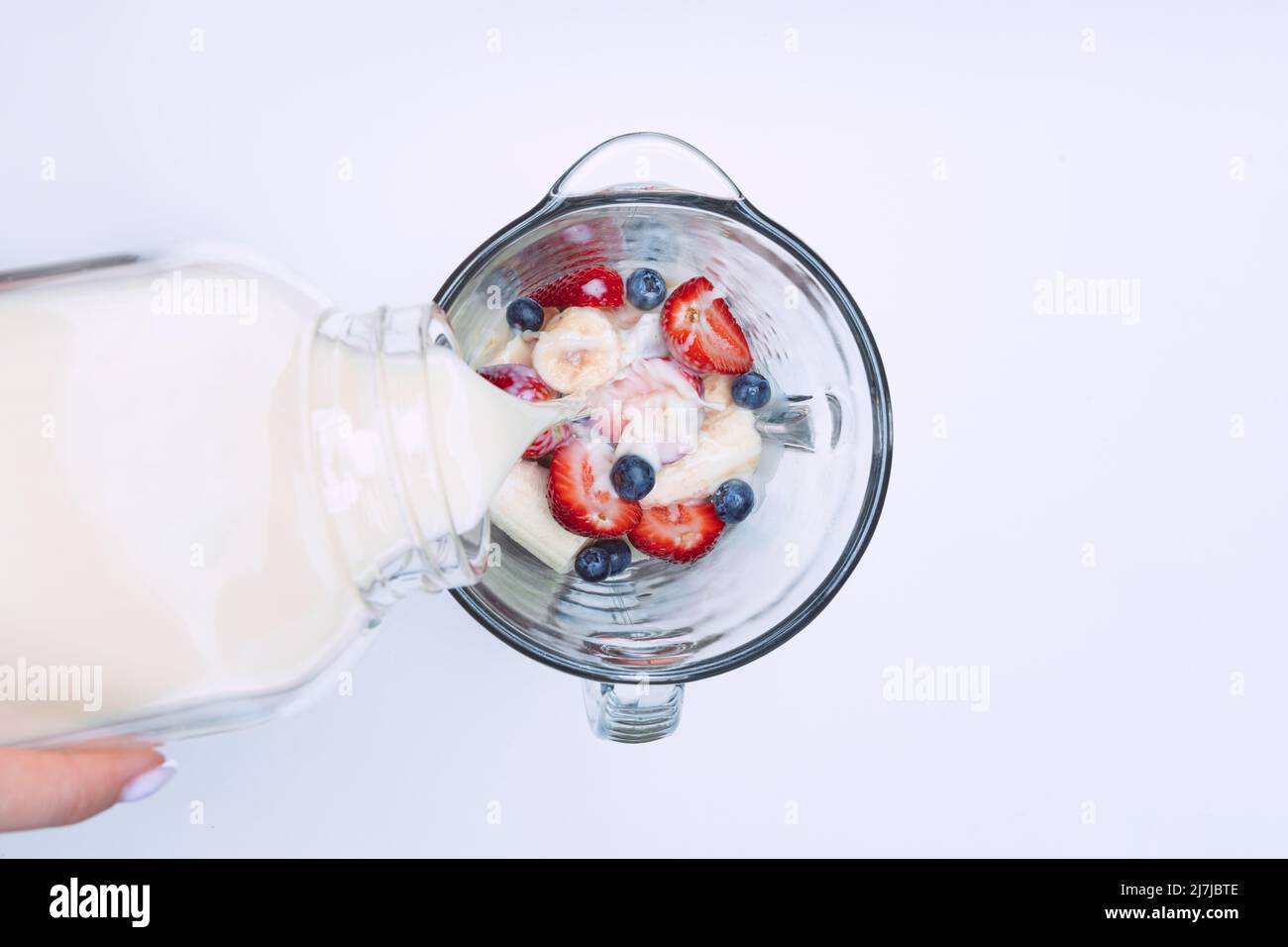 Making smoothie or milkshake in blender. Pouring milk in a blender with fruits. Vegan smoothie with plant based milk Stock Photo