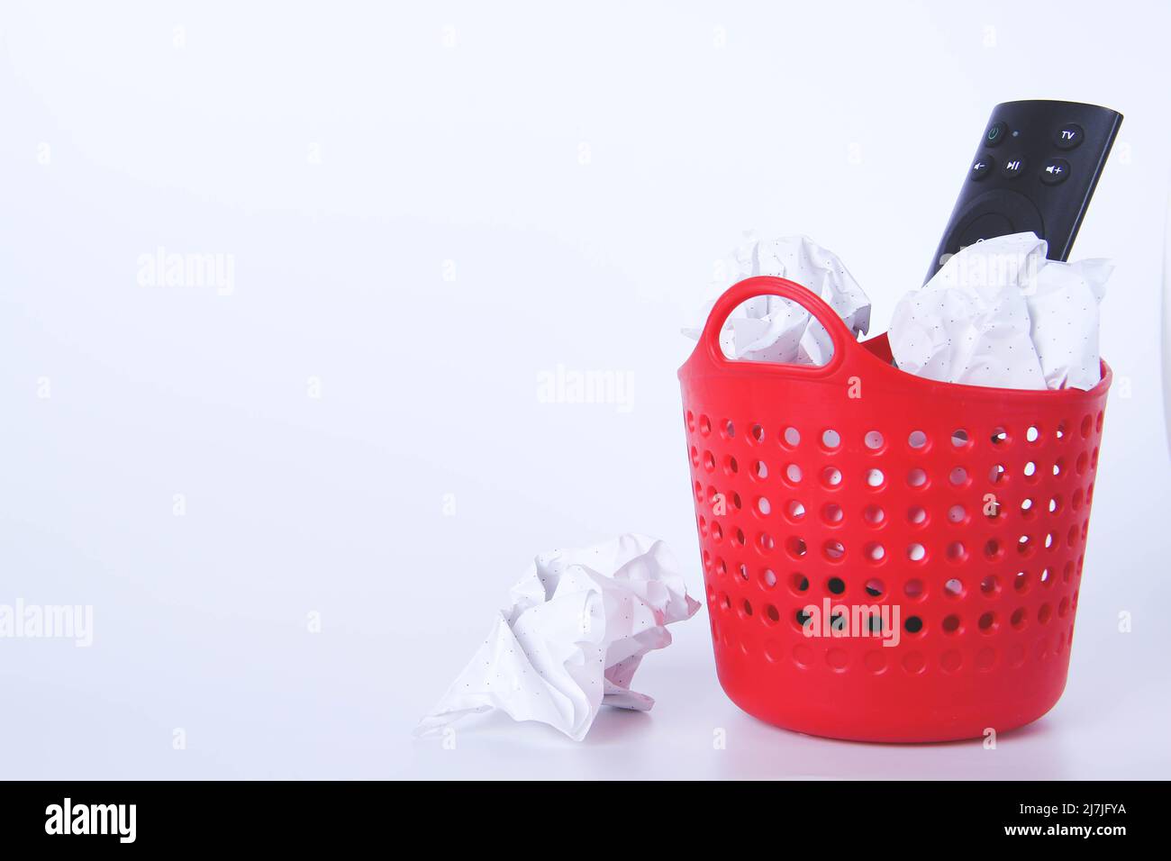 The TV remote is in the trash. Full red trash can. Disposal of