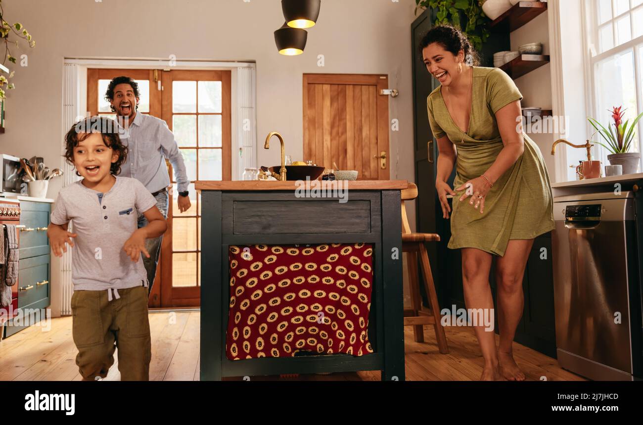Playful parents chasing after their son in the kitchen. Happy young family having fun together during playtime. Mom and dad spending some quality time Stock Photo