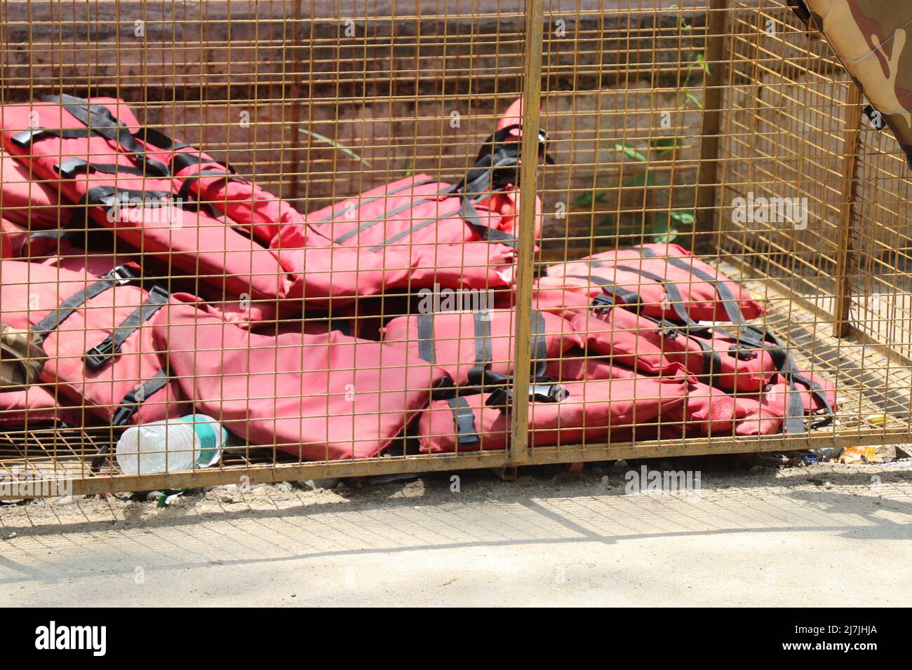 Life jackets in red color kept inside a metal netted container important for protecting life in sea or ocean or water sources Stock Photo