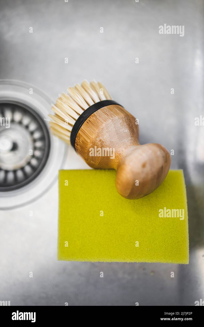 kitchen sink with disposable sponge vs durable reusable bamboo brush to wash the dishes, concept of environmentally sustainable household products Stock Photo