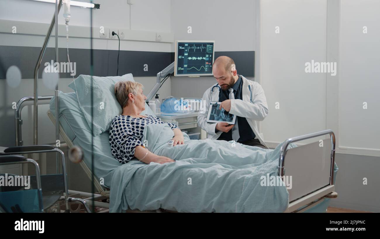Doctor explaining x ray scan results on tablet to aged patient at