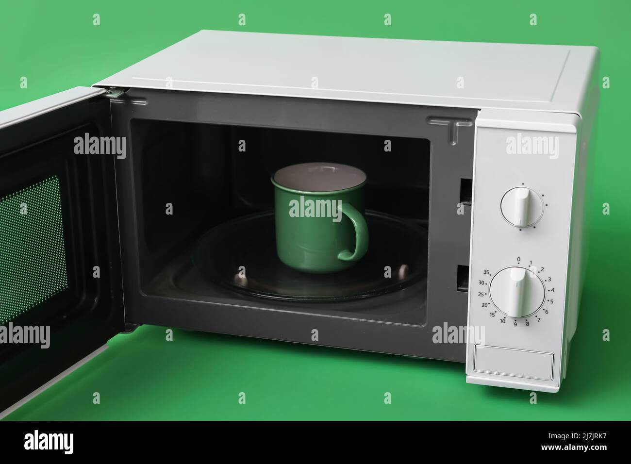 Cup with drink in microwave oven on green background Stock Photo Alamy