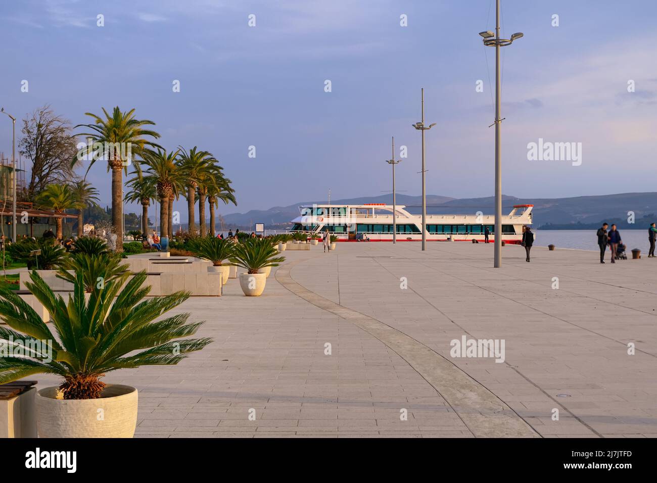 palm trees along beautiful promenade coast ferry and people silhouettes walking around. relax and calm world places Stock Photo