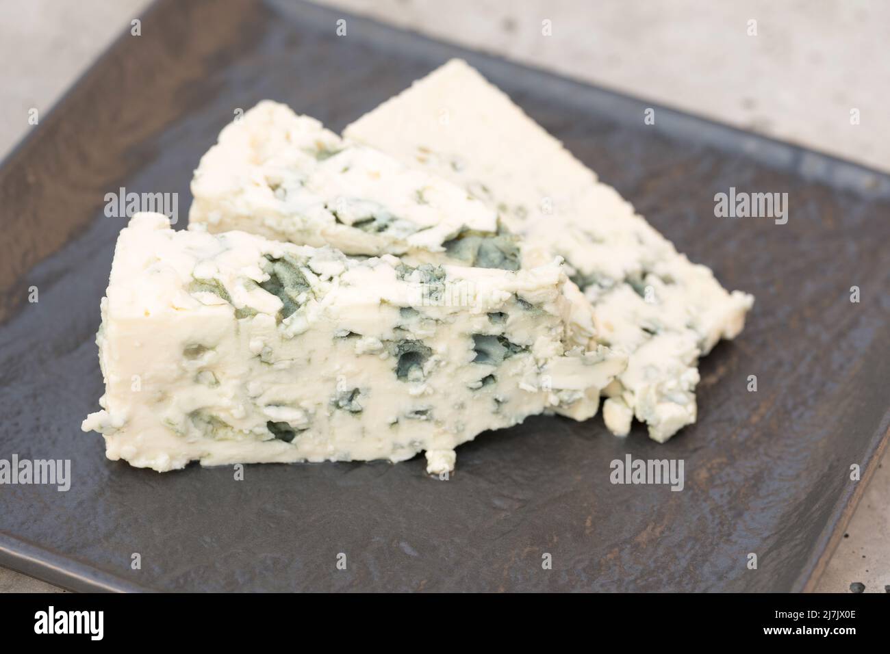 Dorblu cheese with blue and green mold veins on black serving plate. Consistency of blue cheese. Traditional antipasti, classic blue mould cheese Stock Photo