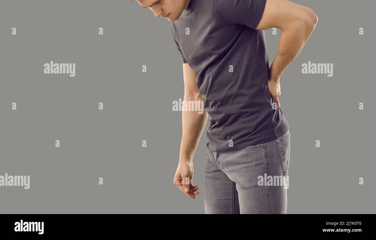Young man suffering from back pain due to large physical exertion isolated on gray background. Stock Photo