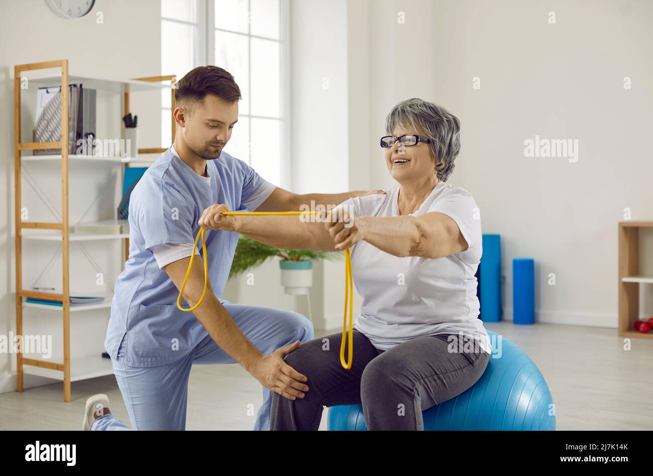 Physiotherapist helping senior woman with osteoporosis to do exercises on fitball Stock Photo