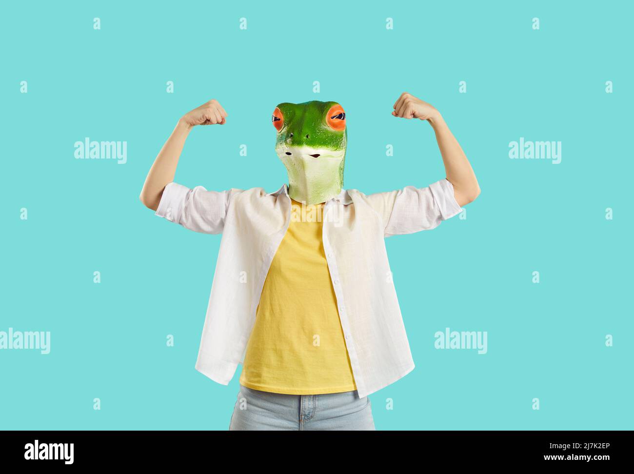 Young woman with funny frog head mask shows her strength isolated on bright light blue background. Stock Photo