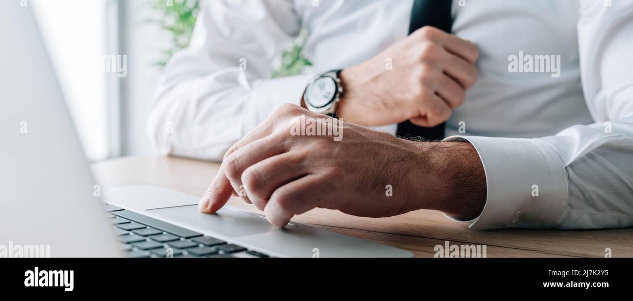 Businessman using laptop computer at office desk, hand on a trackpad or touchpad, panoramic image with selective focus Stock Photo