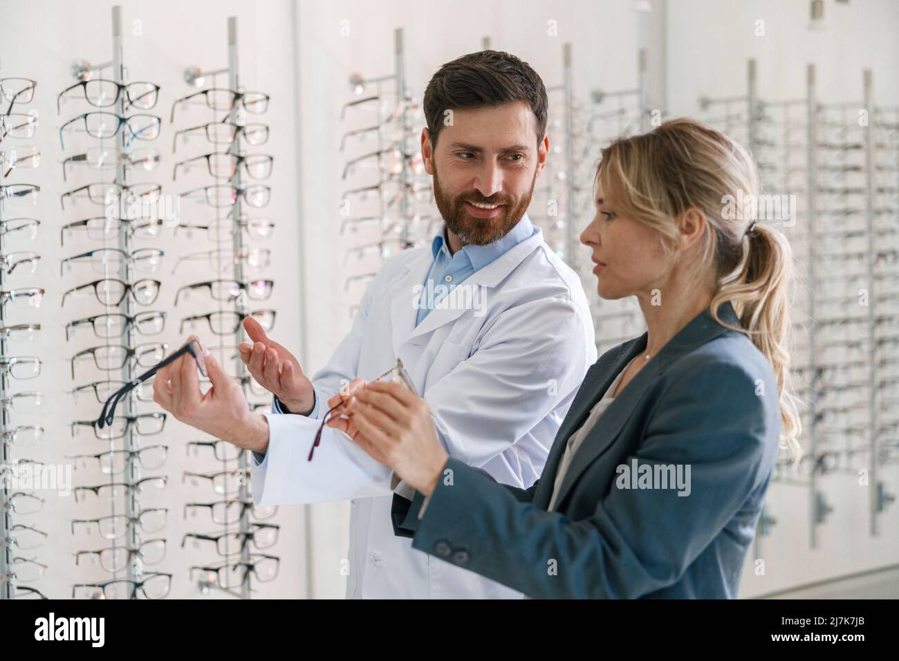 The ophthalmologist helps the client to choose a more suitable spectacle frame in optical store Stock Photo