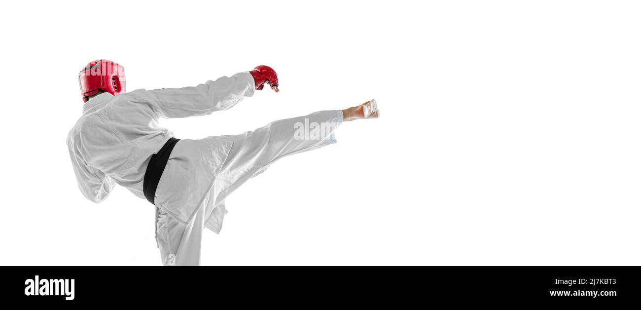 Back view. Portrait of young sportive man wearing white dobok, helmet and gloves practicing isolated over white background. Concept of sport, workout Stock Photo