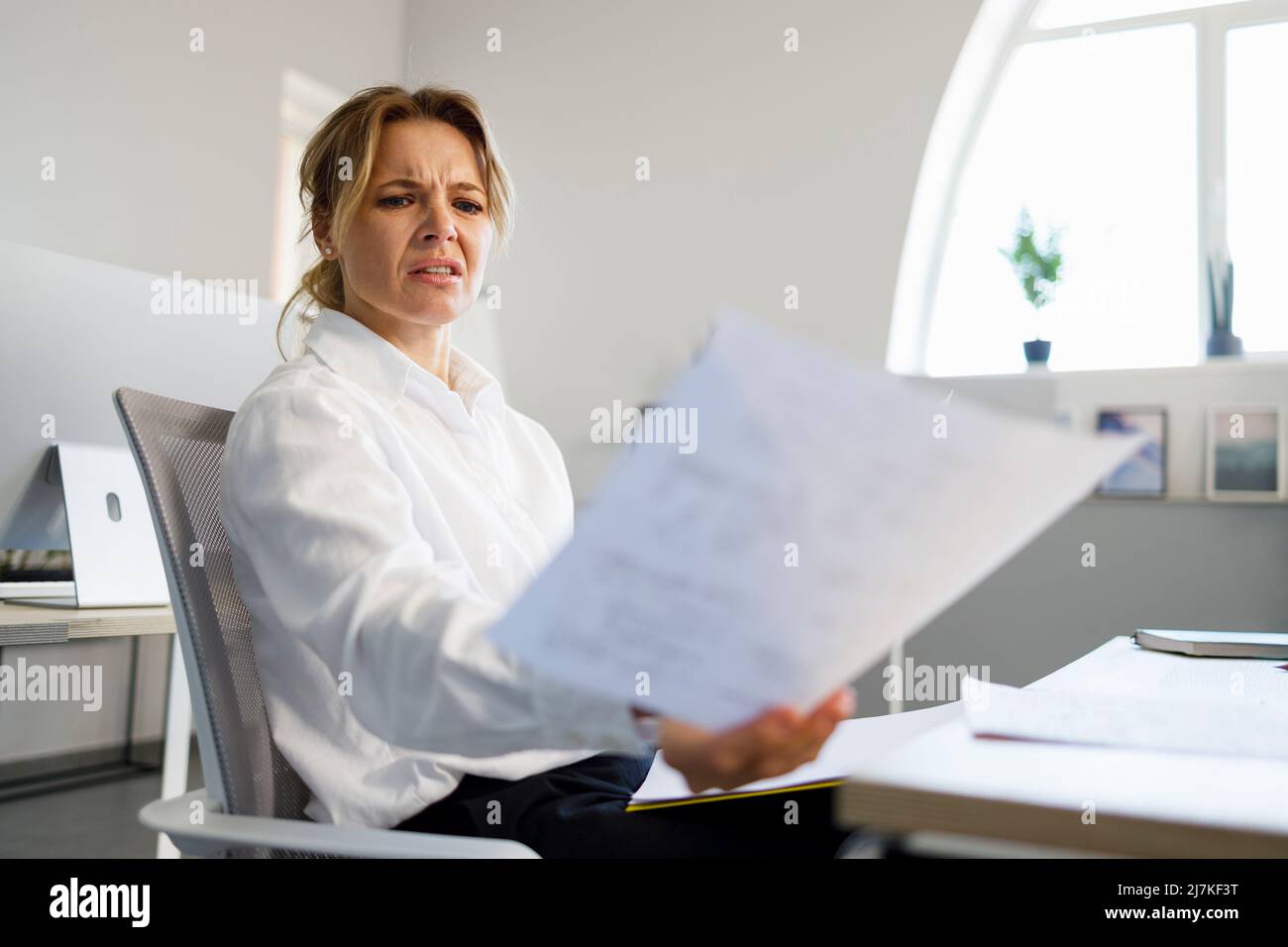 Dissatisfied business woman examines documents at her workplace in office Stock Photo