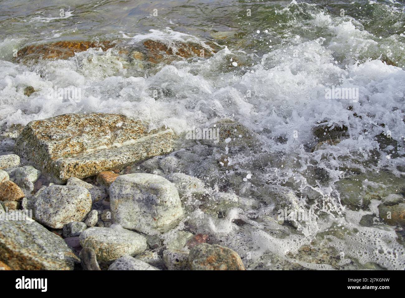 Wave splashing on the rocky beach with foam Stock Photo