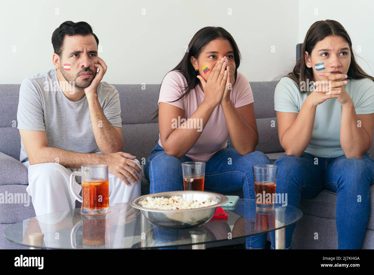 Soccer fans cheering on the national team at home. Sitting on the sofa and drinking Stock Photo