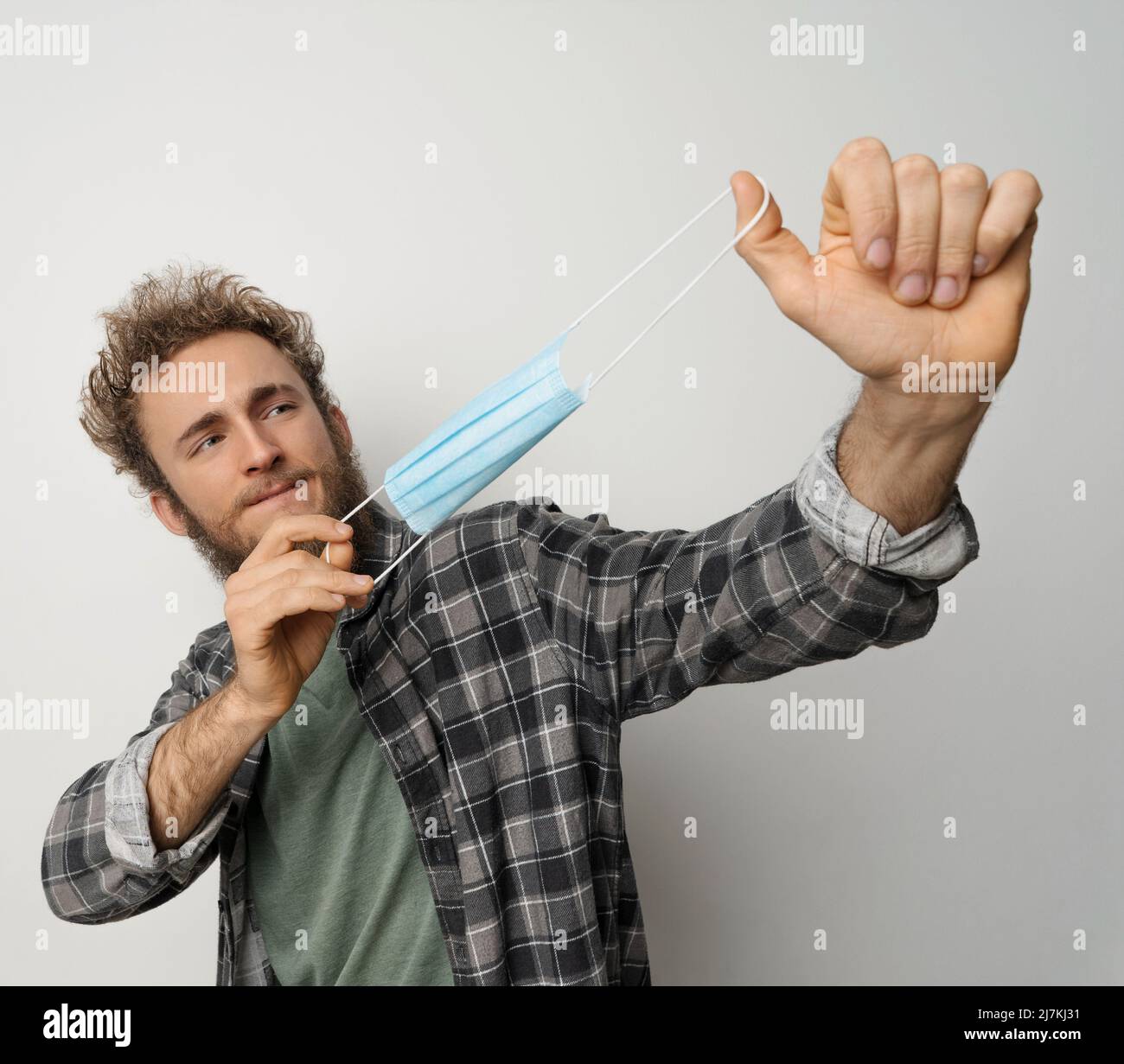 Tired of face mask young man in plaid shirt pops it in the air. Happy handsome anti mask guy. Exhausted young man trying to rid of medical mask. Health care concept. Covid 19 concept. Stock Photo