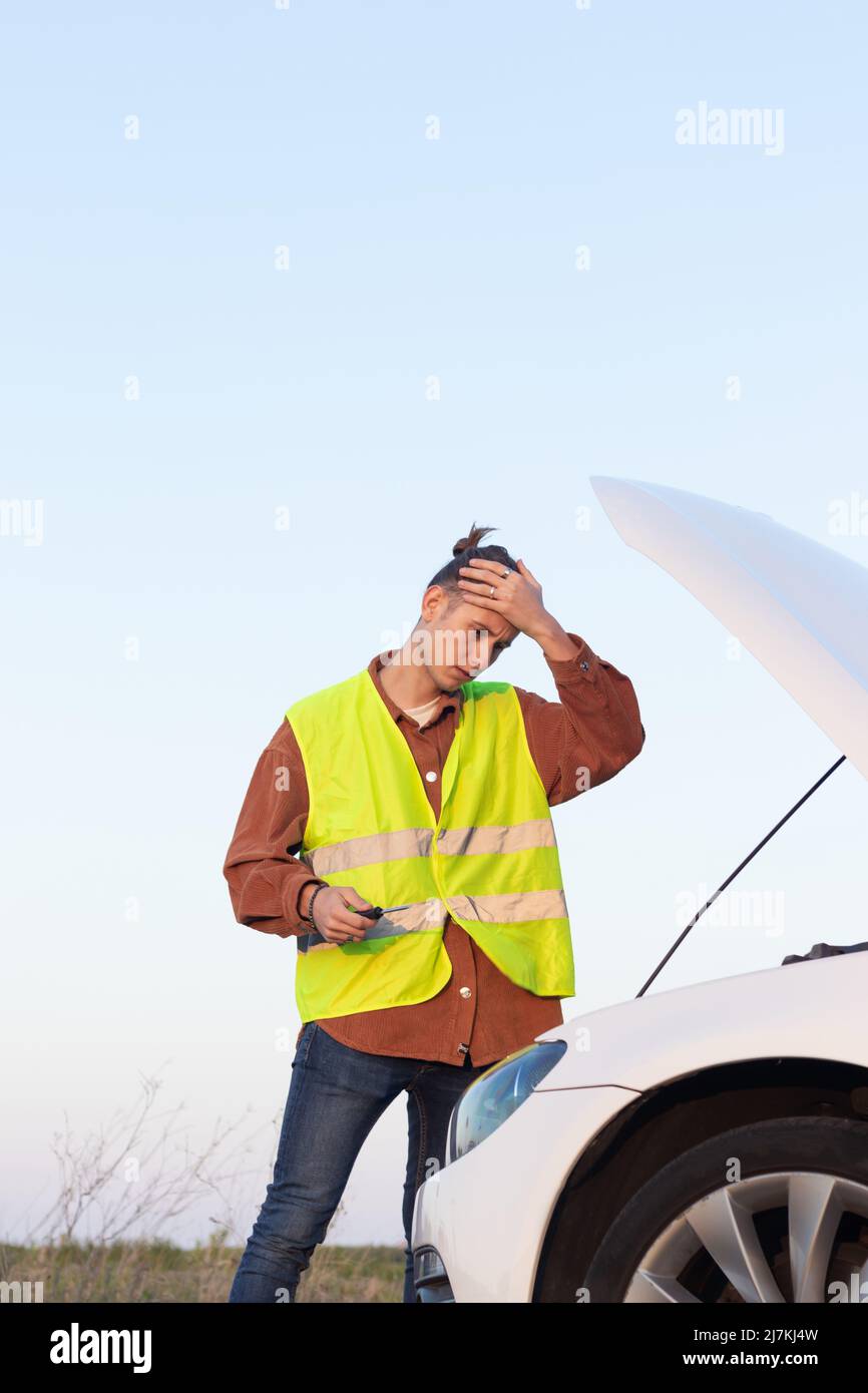 Tired man with problems tries to repair a broken car with the open hood ...