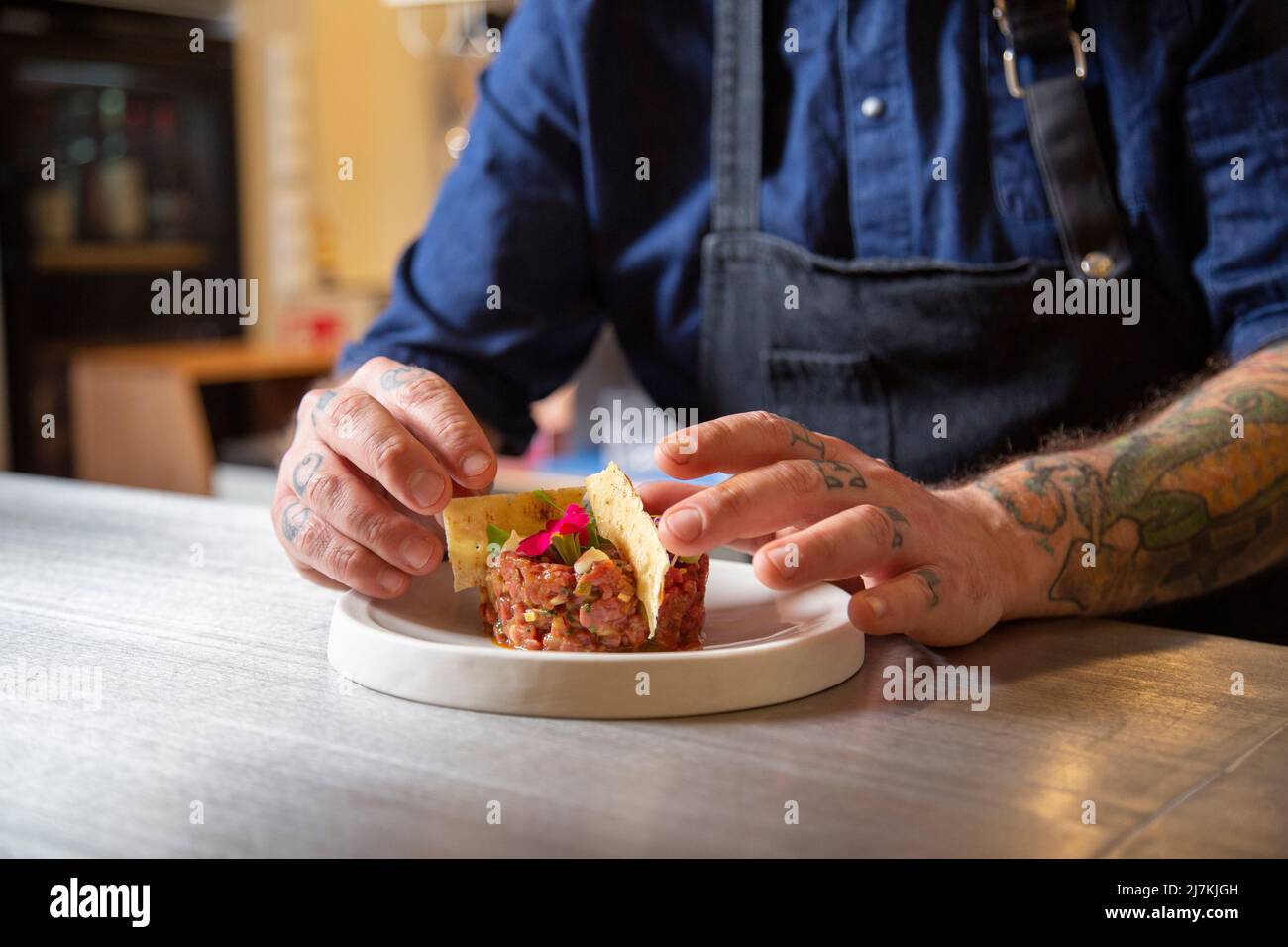 Crop anonymous tattooed male chef in apron putting crackers in fresh ...