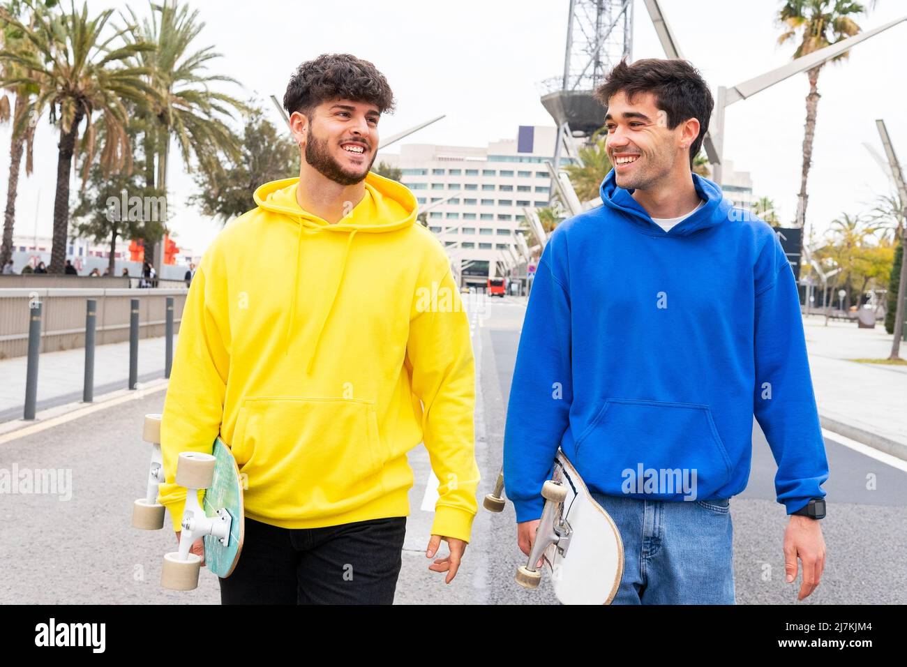 Two cheerful friends skaters wearing blue and yellow sweaters walking in the streets of Barcelona, Spain Stock Photo