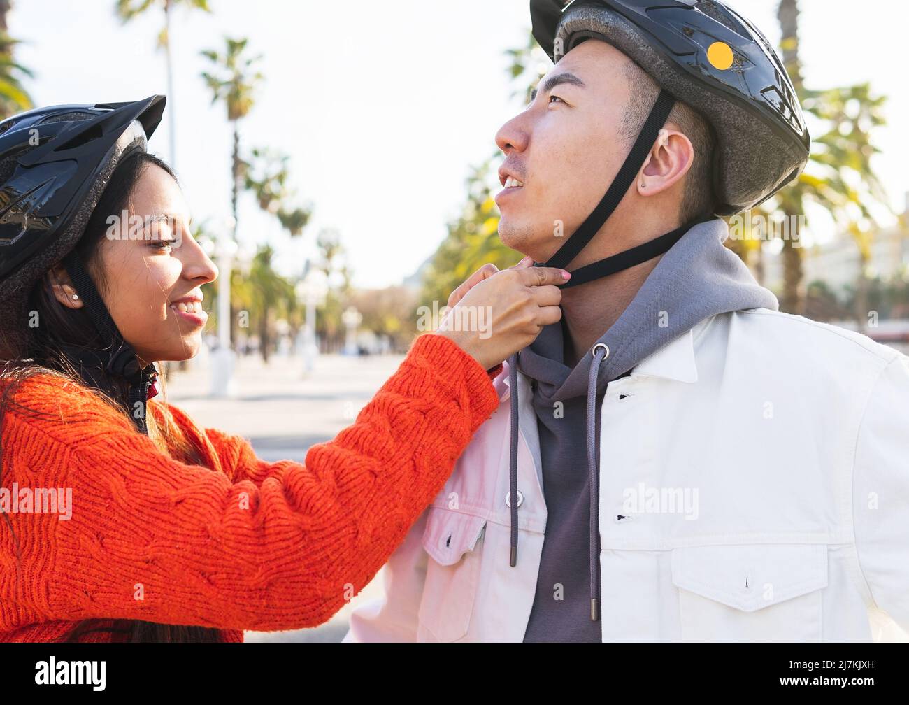 Side view of positive Indian girlfriend fastening protective helmet on