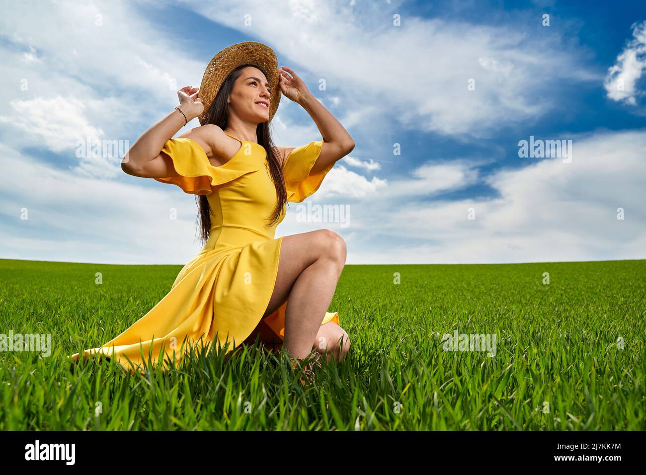 Young woman in yellow dress and straw hat on a green wheat field in ...