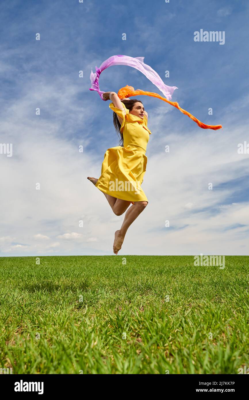 Action shot of a young attractive woman in yellow dress jumping for joy ...