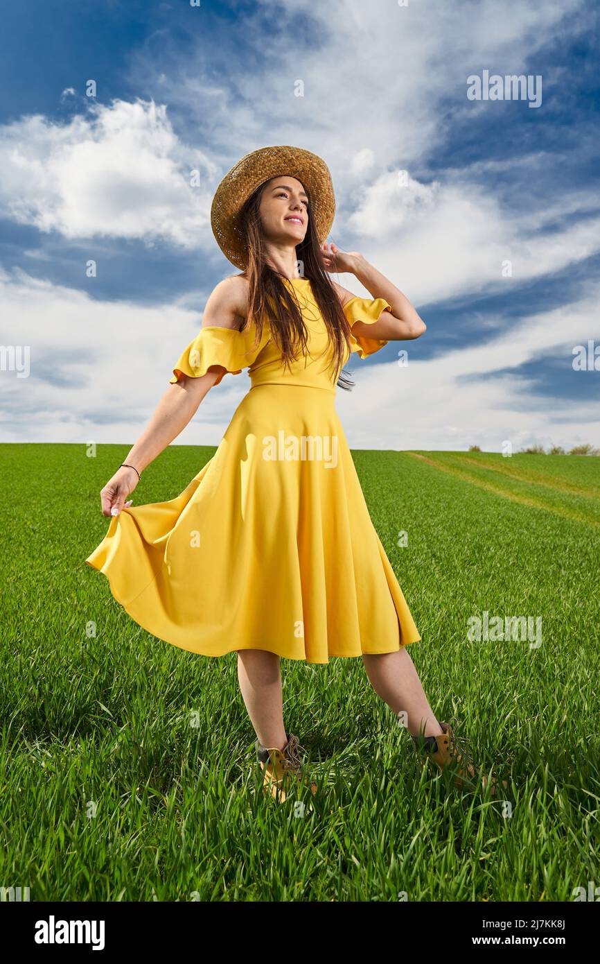 Young woman in yellow dress and straw hat on a green wheat field in ...