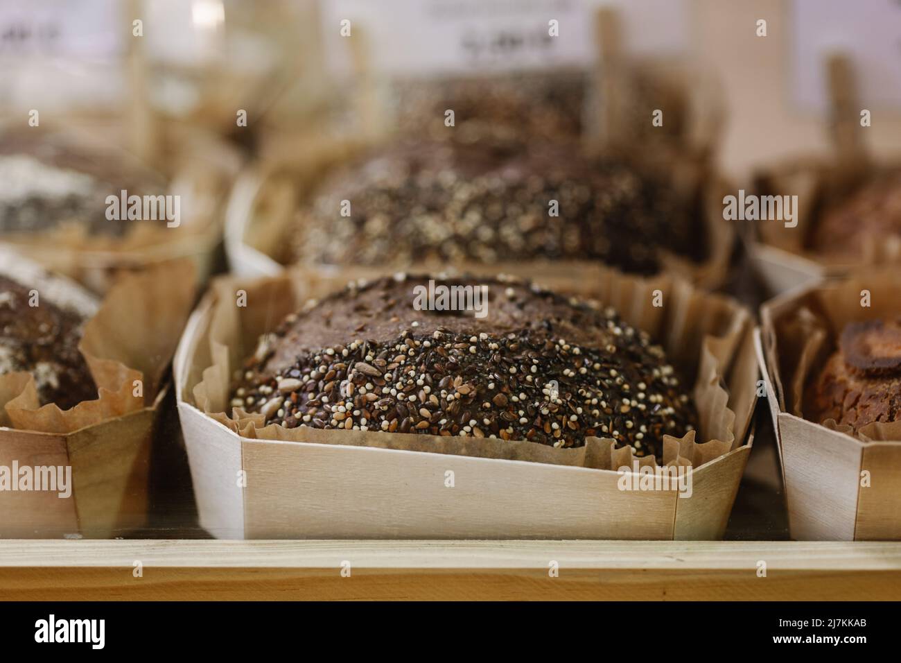 Soft focus of loaves of fresh rye bread in paper containers placed behind shop window of bakery Stock Photo