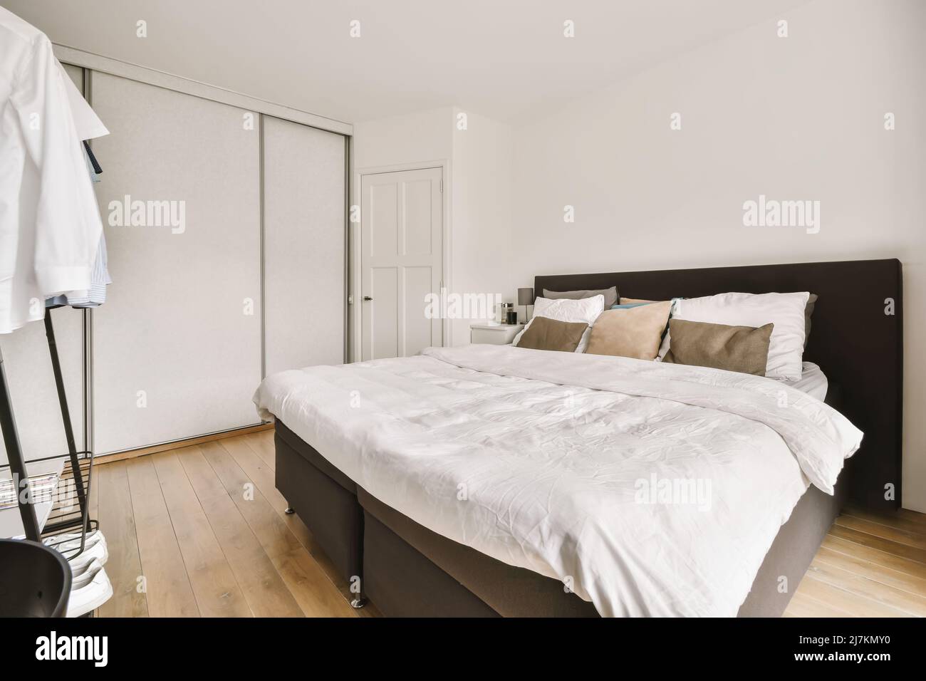 Comfortable white bed near various garments placed in light modern