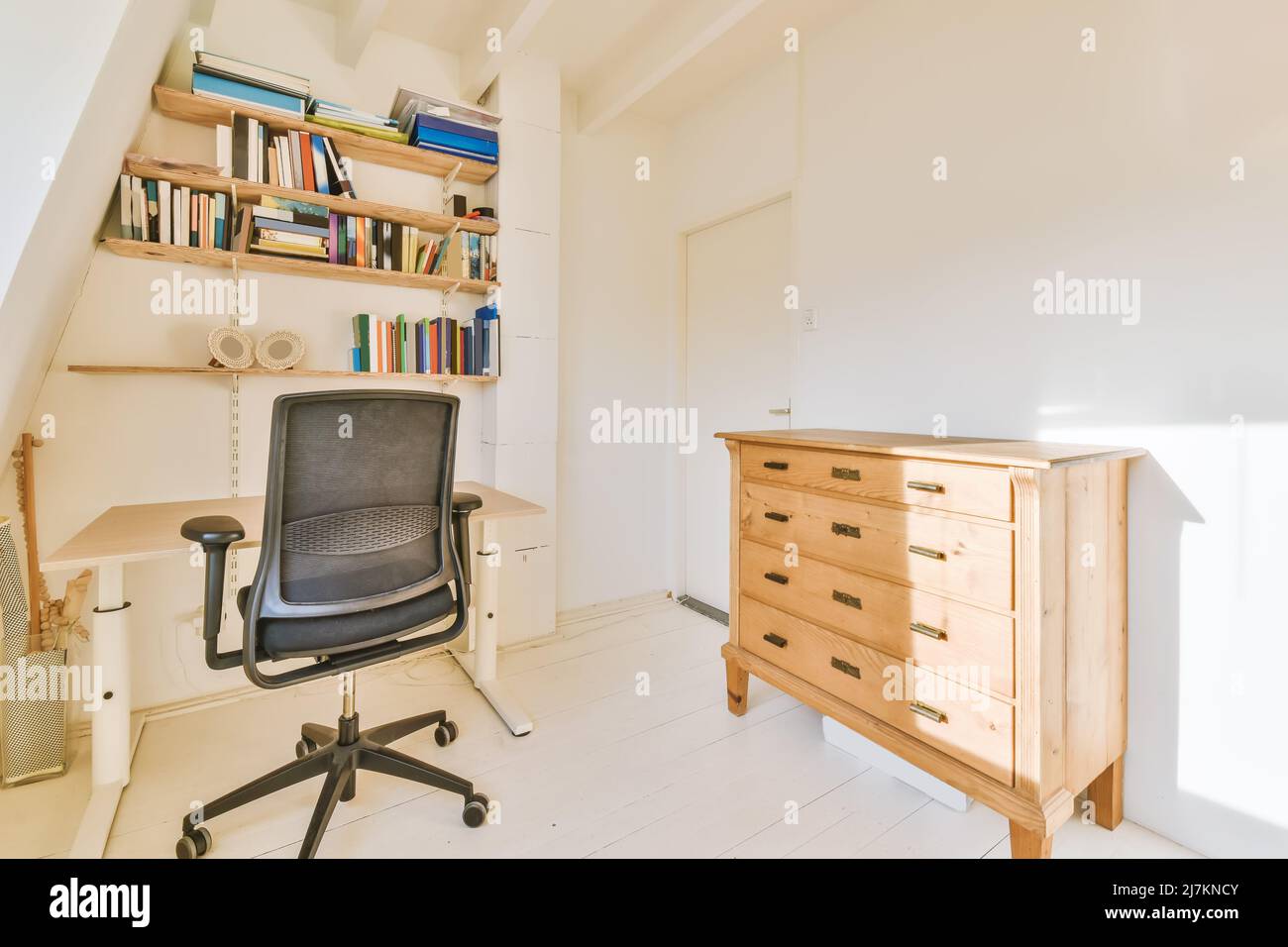 Chair at table placed in sunny study room with bookshelf and chest of drawers Stock Photo