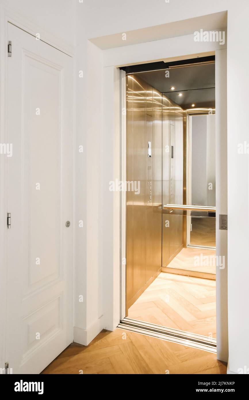 Modern elevator with opened door and mirrored wall in hallway of apartment building with wooden parquet floor Stock Photo