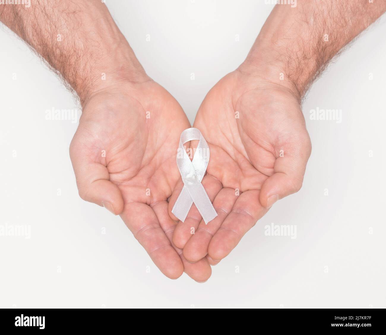 White awareness ribbon. Lung cancer awareness white ribbon bow on man hands. Anti violence against women. Medical and political awareness symbol. Healthcare concept. Political movement concept.  Stock Photo