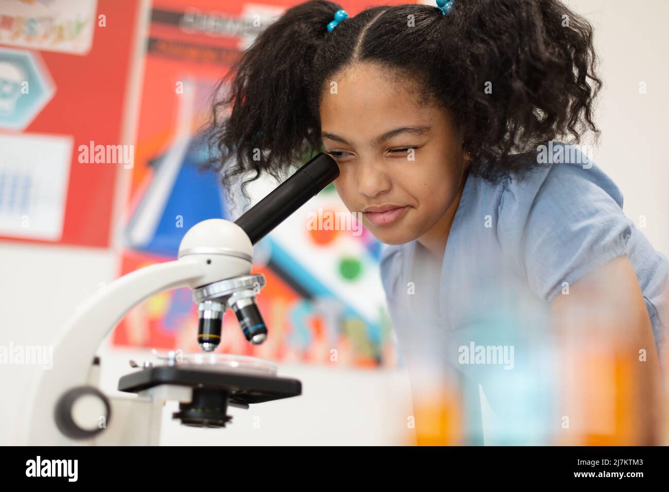Biracial elementary schoolgirl looking through microscope during