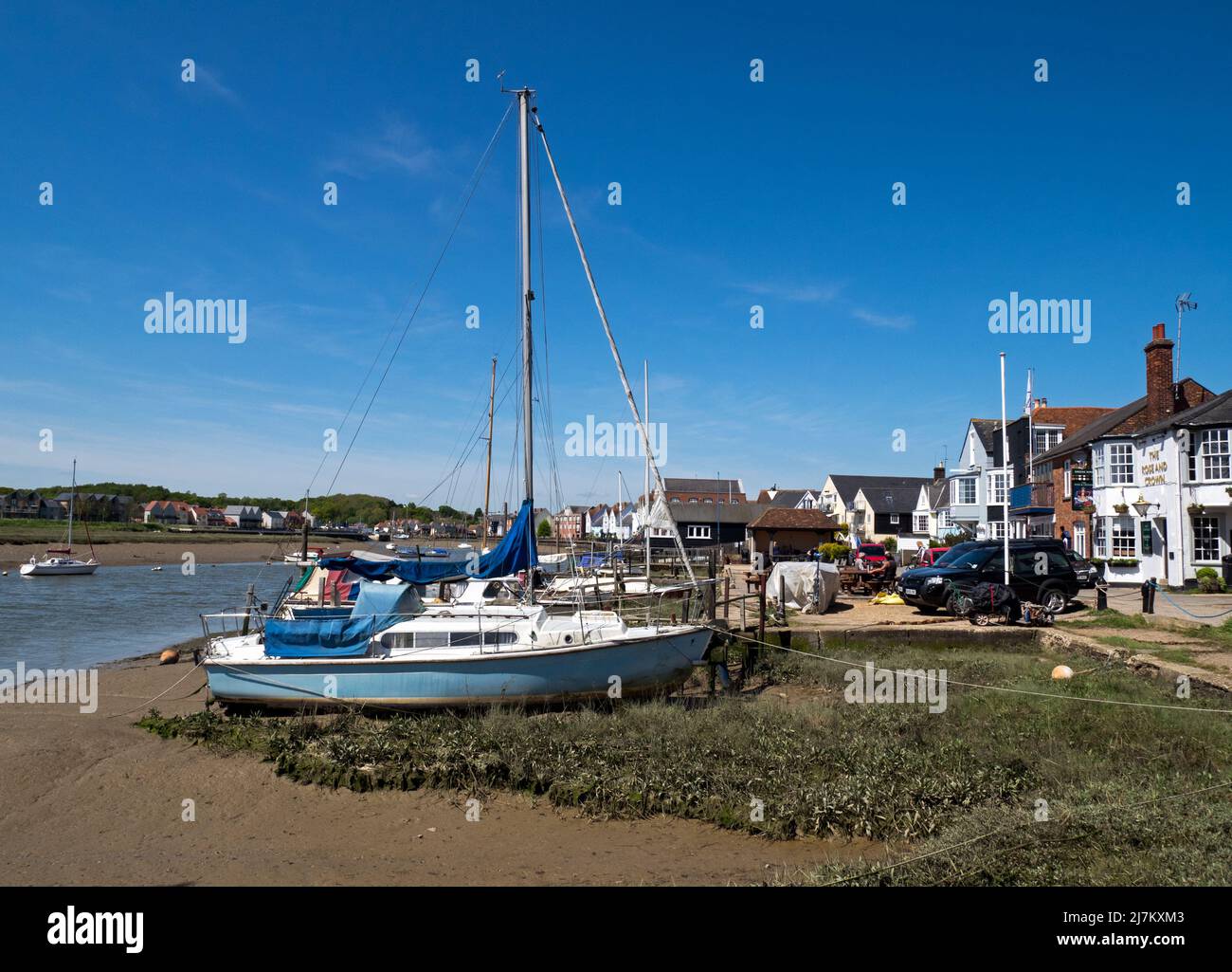 Sailing boats moored on the beach front of the estuary of the River Colne along with the building of the ancient town of Wivenhoe, Essex, England, UK Stock Photo