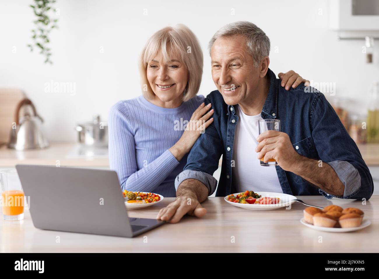 Happy senior couple using computer while having breakfast Stock Photo