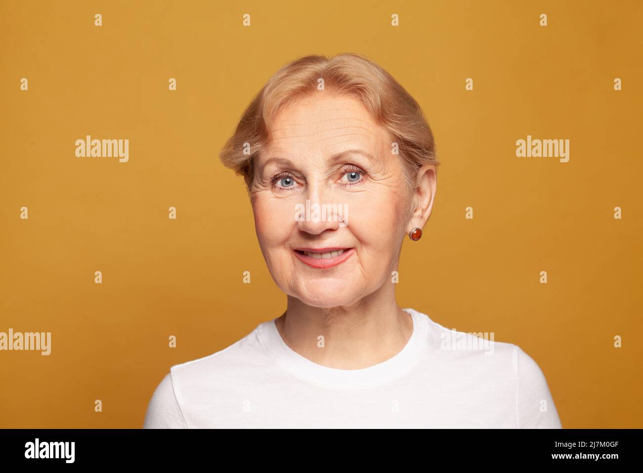 Cute friendly senior woman face on bright yellow studio background