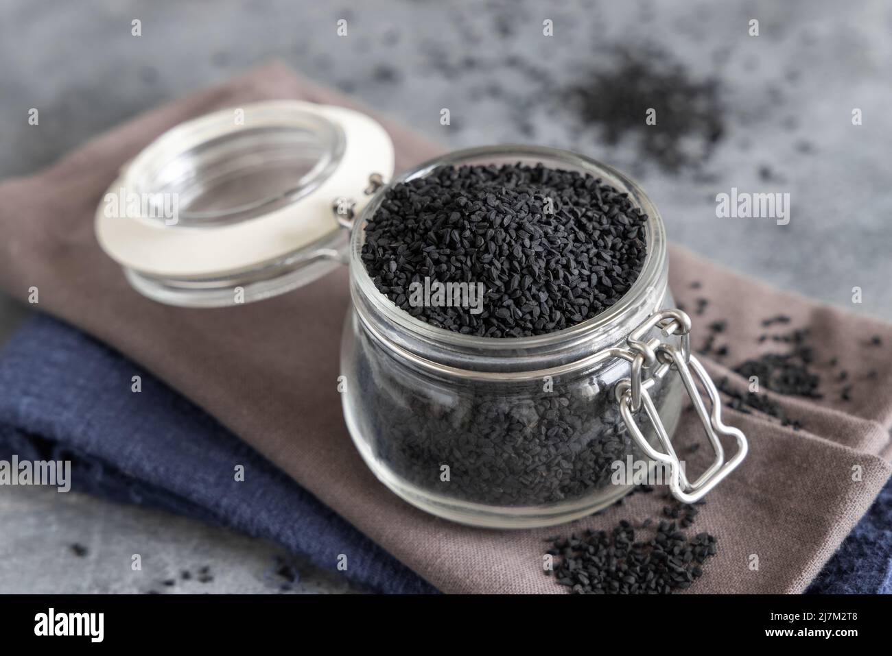 Indian spice Black cumin (nigella sativa or kalonji) seeds glass jar on grey table close up with  copy space Stock Photo