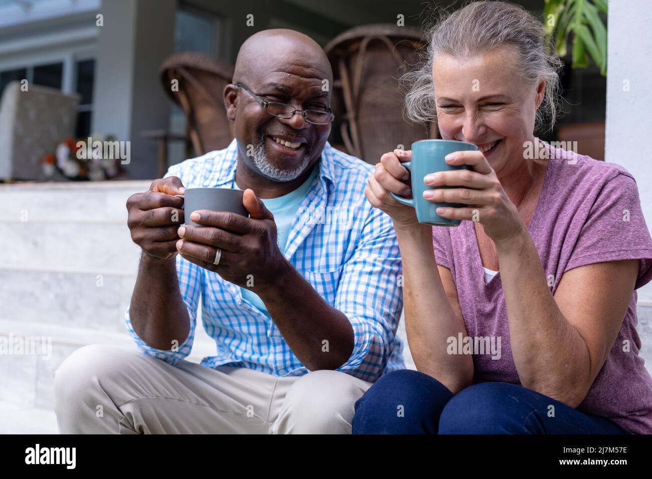 Happy multiracial senior couple having coffee together while sitting on ...