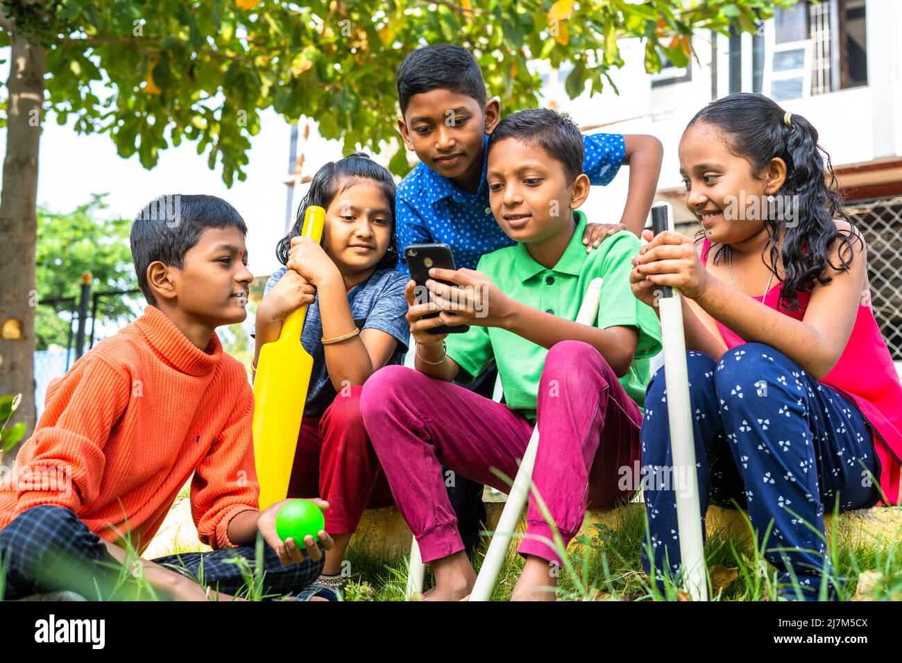 Teenage kid showing mobile phone to his friends at park after playing cricket - concept of technology, togetherness and communication Stock Photo