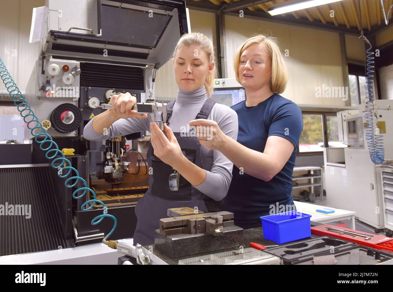 A young trainee receives tuition from her trainer. Both women work as computerized  numerical control engineers. They are seen  together at their high Stock Photo