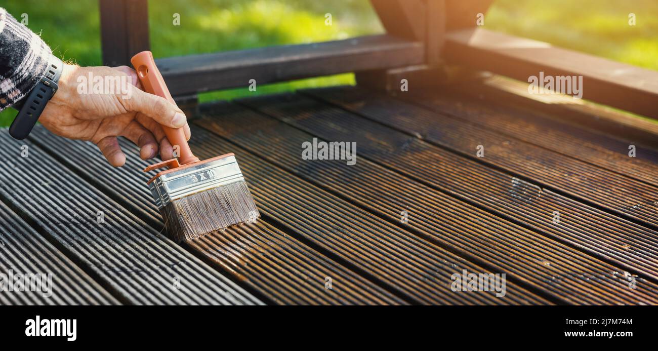 restore wooden terrace planks. applying wood protection oil on decking boards with paint brush. copy space Stock Photo